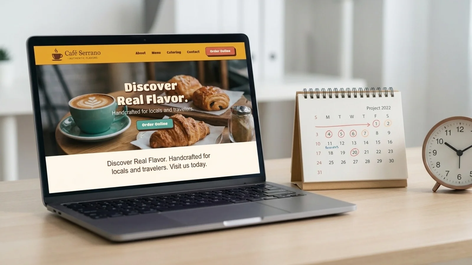 A laptop showing a café website next to a desk calendar with dates circled and an analog clock